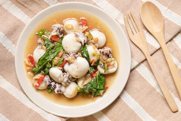 Stir fried Cuttlefish or Cuttlefish Rainbow with basil on table mat with wooden spoon and fork; top view. Thailand's popular dishes (Pad Ga Pow).