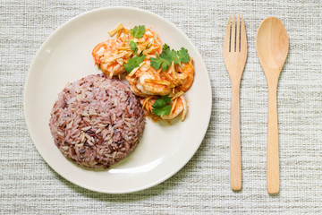Stir fried shrimp with garlic and coriander leaves serve with cooked mix riceberry, jasmine rice, brown rice and red rice. Top view with spoon and fork.