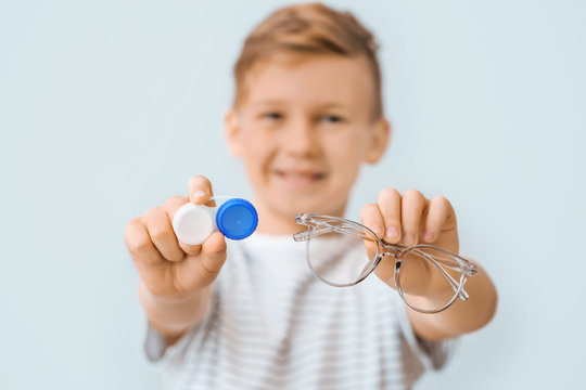 Little boy with contact lens case and eyeglasses on grey background, closeup