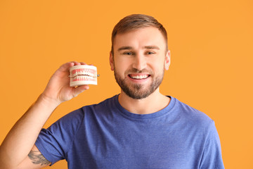 Happy smiling young man with plastic model of jaw on color background