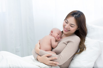 Obraz na płótnie Canvas Beautiful mom supports and tenderly cuddles the newborn baby gently while the infant is sleeping on the chest. Asian mother looking at the baby with love and showing protection.