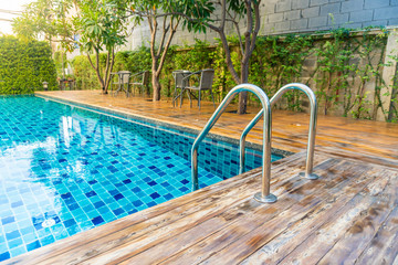Swimming pool with stair at hotel with decorated with trees and chairs for relaxing