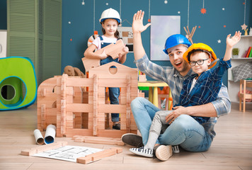 Father and little children dressed as builders playing with take-apart house at home