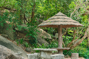 Stone chairs under the shady cover made of straw in the public park