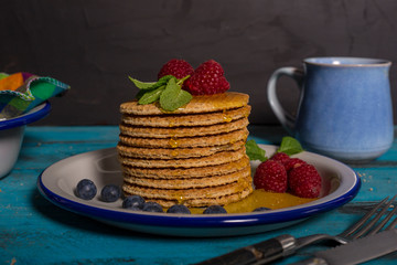 Close-up of a stack of Dutch waffles with raspberries, blueberries and honey on blue wooden background. Isolated image.