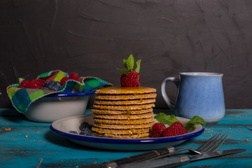 Breakfast table. Dutch waffle dish with raspberries, blueberries and honey with cutlery on blue wooden background. Isolated image. Breakfast concept