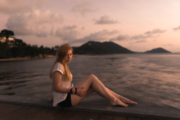 Beautiful girl at sunset on the sea in Thailand. Bright orange and yellow pink sky. Girl traveler enjoys the view. Woman in the tropics