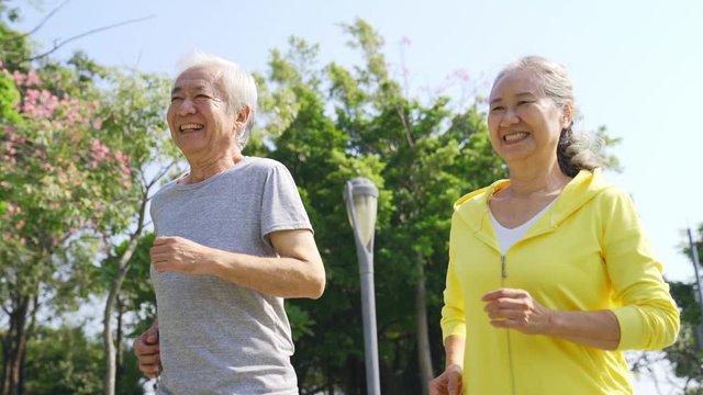 happy senior asian couple jogging running exercising outdoors in a park