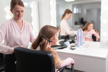 Obraz premium The work of the stylist on hairstyles in a bright salon, the girl makes curls and braids braids of a small beautiful model,