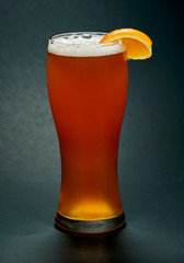 Glass of red beer with orange slice over black background.