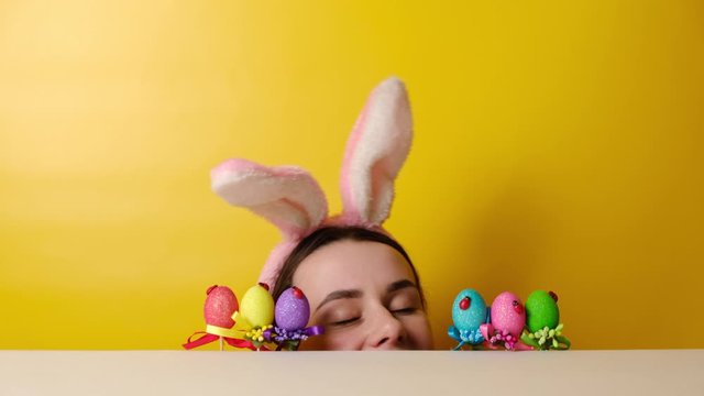  Charming cheerful happy young woman begin to hunt for Easter eggs, wears fluffy ears, poses over yellow background with copy space. Seasonal holiday concept. Happy easter!