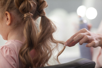Fototapeta premium The work of the stylist on hairstyles in a bright salon, the girl makes curls and braids braids of a small beautiful model,