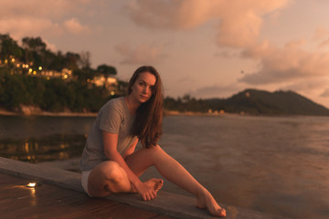 Beautiful girl at sunset on the sea in Thailand. Bright orange and yellow pink sky. Girl traveler enjoys the view. Woman in the tropics