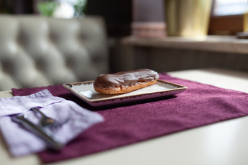 Eclair on a plate and purple napkin in a beautiful vintage interior, cafe