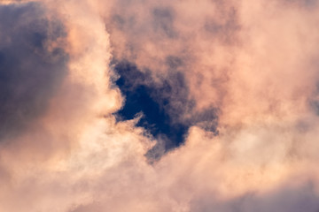 Fototapeta na wymiar Close up of storm clouds colored in sunset colors; break in the clouds reveals dark blue sky