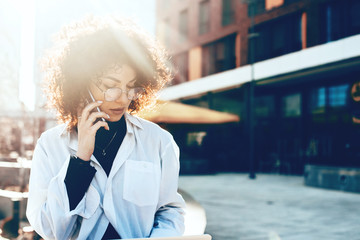 Stunning caucasian woman with curly hair and eyeglasses is wearing a white shirt and having a phone discussion