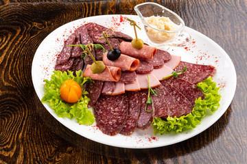 sausage sliced on a white dish with olives and salad on a wooden background