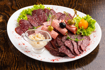 sausage sliced on a white dish with olives and salad on a wooden background