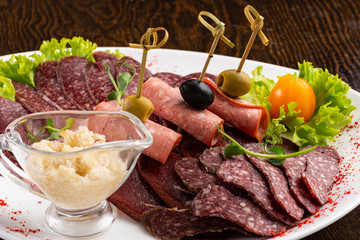 sausage sliced on a white dish with olives and salad on a wooden background