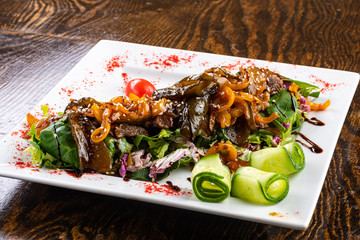 salad with meat, eggplant and vegetables on a white dish on a wooden background