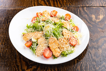 salad with meat, cheese, vegetables, mayonnaise, herbs on a white plate with a spoon on a wooden background