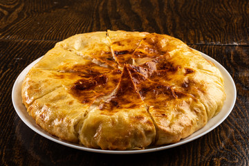 baked pie with cheese sliced in pieces on a plate on a wooden background