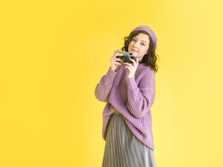 Obraz premium Fashionable girl in a lilac sweater and beret with a retro camera in her hands. Yellow background