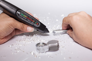 Diamonds on tweezers with testing machine on a white background, reflections on the ground....