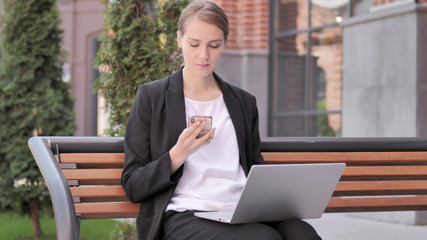 Young Businesswoman Using Smartphone and Laptop, Sitting on Bench