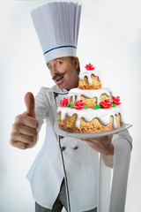 Cook with a large, delicious cake on a plate, with his hand outstretched and finger up