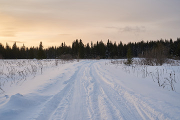 Naklejka premium Snow- covered lake at dawn with boats on the shore. Winter forest with snow-covered fir trees high in the mountains. Sunny February day in the spruce forest. 