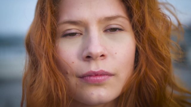 Redhead young woman portrait. Close up portrait young beautiful student looking at camera real people, feminine beauty wind blows young woman's hair