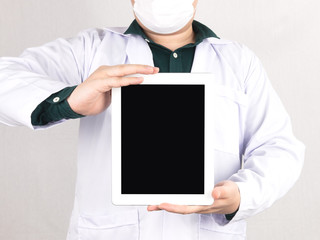 Close up of male doctor wearing uniform and protective face mask, hands holding blank screen digital tablet. Medical and healthcare concept