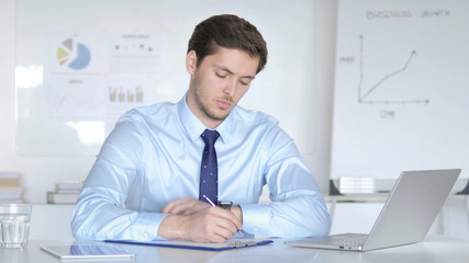 Thoughtful Young Businessman Writing in Office