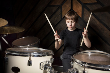 A boy is playing with a drumstick. The child behind the drum kit.