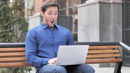 Sitting Outdoor Young Man in Shock Working on Laptop