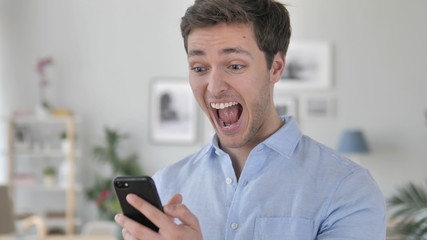 Obraz na płótnie Canvas Excited Man Enjoying Success while Using Smartphone