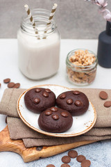 Chocolate cookies with choco drops on white plate, and glass of milk