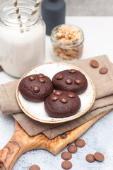 Chocolate cookies with choco drops on white plate, and glass of milk