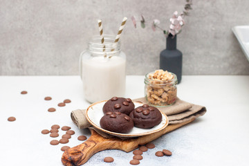 Chocolate cookies with choco drops on white plate, and glass of milk