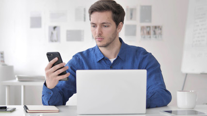 Man Using Smartphone and Laptop for Work
