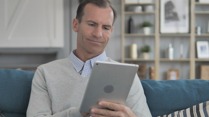 Middle Aged Man Using Tablet while Relaxing on Couch