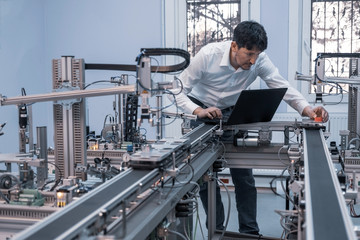 Engineer is working on laptop to program smart factory prototype's automation. automated car on production line, artificial intelligence in smart manufacturing. Industry 4.0 concept.
