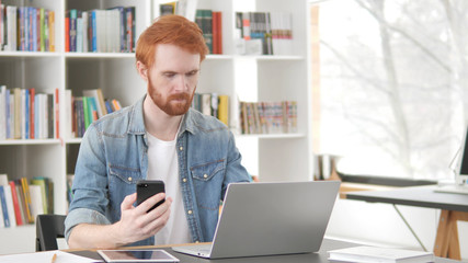 Young Casual Redhead Man Using Phone and Laptop