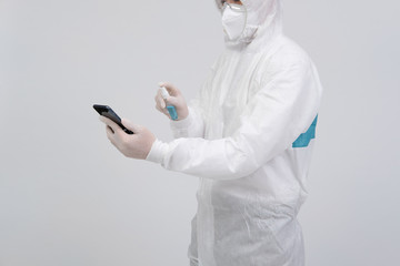 man wearing biological protective uniform suit clothing, mask, gloves spraying sanitizer on smartphone for sanitizing virus bacteria