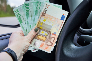 Euro banknotes of various denominations in a woman hand inside of a car