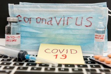 2019 Coronavirus write on vedical mask with vaccine in ampoule and laptop. Worldwide epidemic. Virus vaccine search concept.