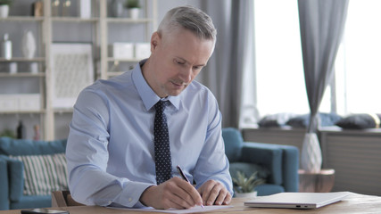 Gray Hair Man Talking on Phone while Working on Laptop