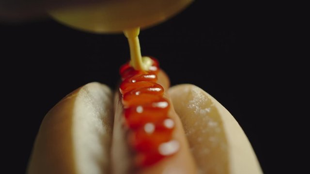 CLOSE UP: Yellow mustard sause poring on a hot dog with sausage and ketchup sauce from a bottle.