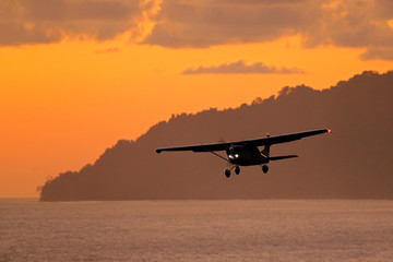 Fototapeta na wymiar Aircraft on the orange sky with dark clouds. Airplane in the wil nature. Forest hill near the ocean water. Air travelling in Costa Rica. Evening sunset in sea coast of Corcovado NP, Costa Rica.